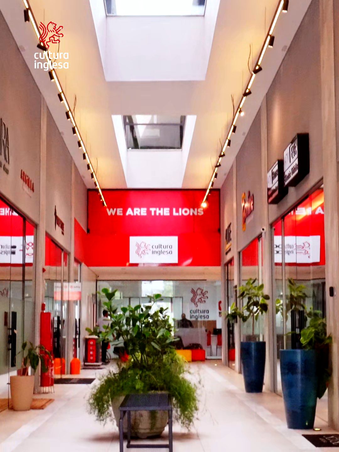 Entrada da Cultura Inglesa Resende, com painel vermelho escrito We Are The Lions ao fundo